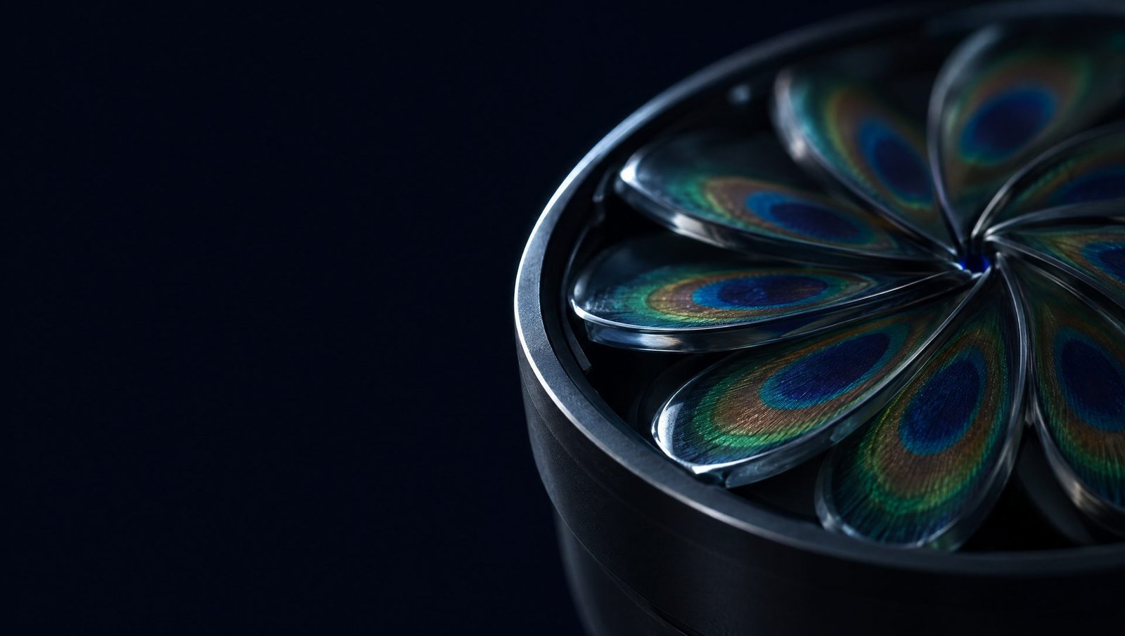 A dark titanium lens barrel in low light, its nine glass blades, each set with a peacock-feather ocellus, closed almost shut.